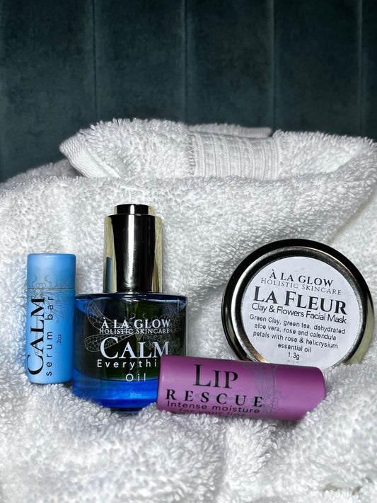 Set of skincare products including 'Calm' serum, oil, and lip rescue on a textured white surface.